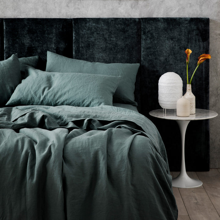 A bed dressed in Bluestone bed linen, styled with a velvet headboard, white bedside table, two ceramic vases and a white lantern lamp. Sizes: Single, Double, Queen, King