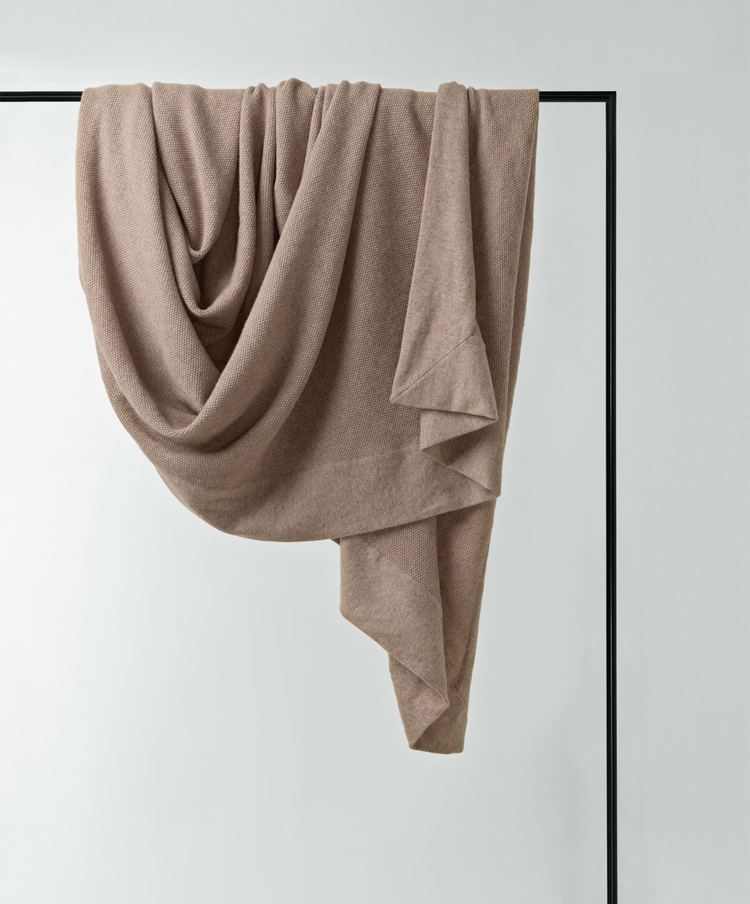 Alba Cashmere Throw in soft beige, draped elegantly on a black metal frame showcasing fine Italian craftsmanship.