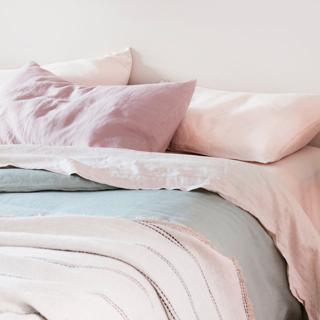 A close up of a bed dressed in Blush, Dusk, Smoke Grey and Sage bed linen styled with a Mira Throw in Ana								