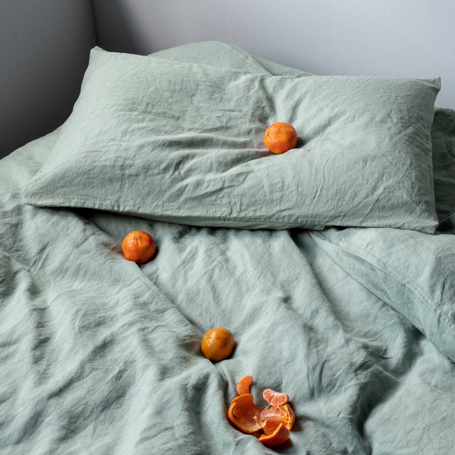 A bed dressed in Sage bed linen, styled with oranges.				