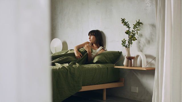 Image shows a model in a bed styled with Cultiver linen bedding. Products are from the Forest collection. 