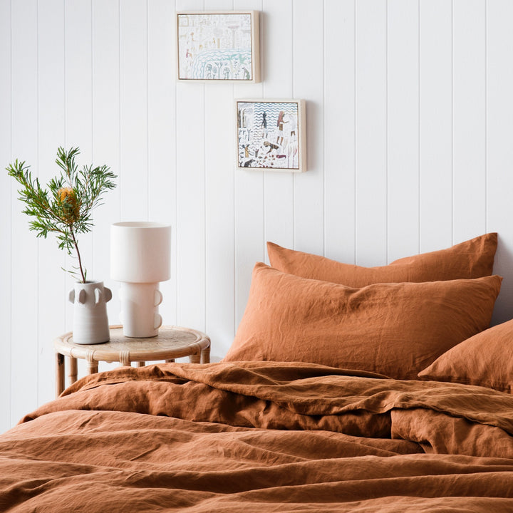 A bed dressed in Cedar bed linen, styled with a bamboo bedside table and vases