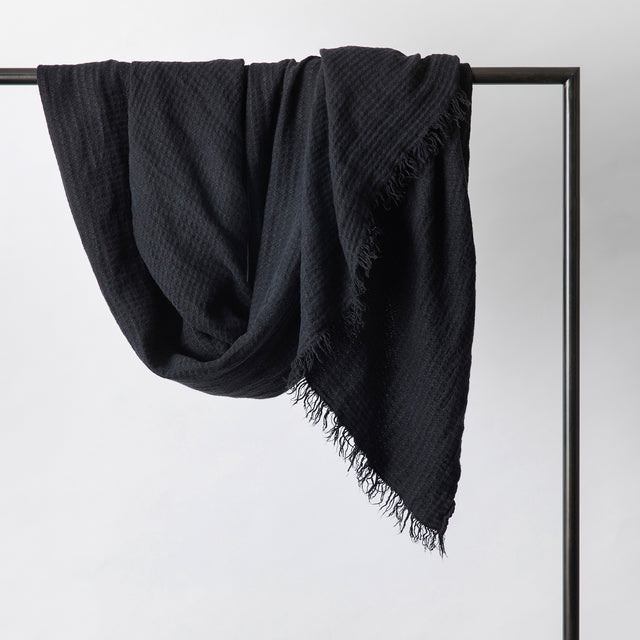 An Estela Linen Waffle Throw in Black hanging on a rail