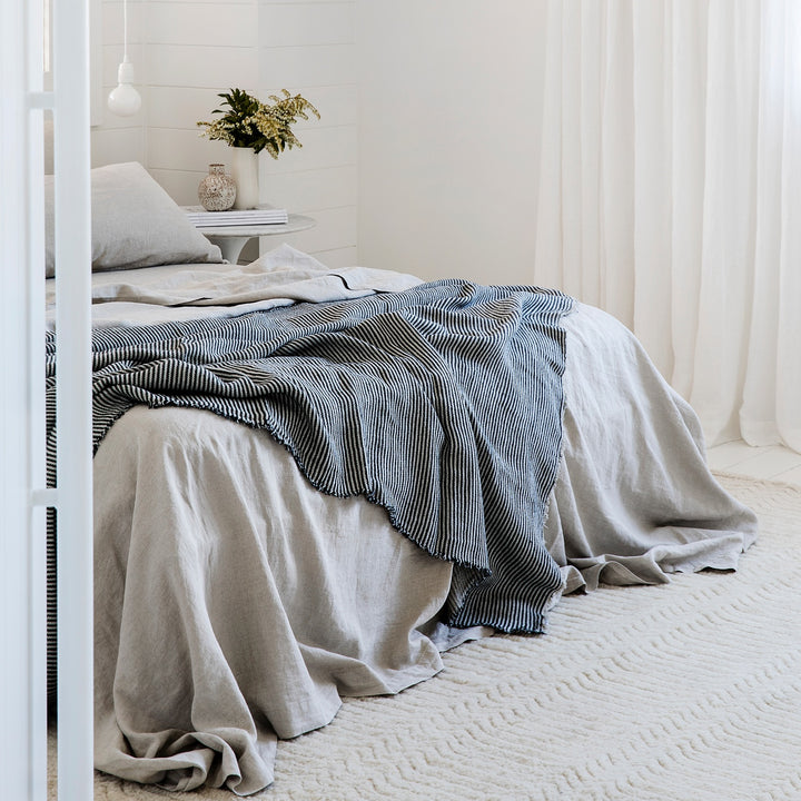  A bed dressed in Smoke Grey bed linen, styled with a Mira Throw in Ellis Stripe