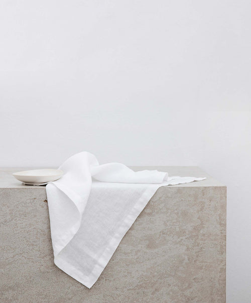 Dining Edit - Natural & White soft European Flax™ linen napkin draped on a neutral stone surface The beauty of home