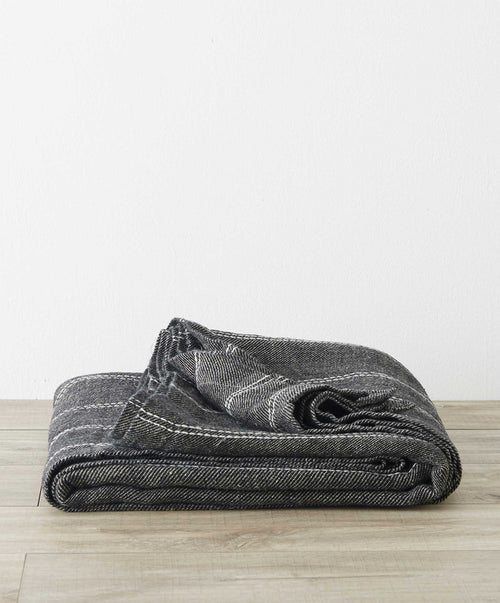 Mira Linen Bedcover - Rafa folded on wood floor showing dark striped natural linen fabric The beauty of home