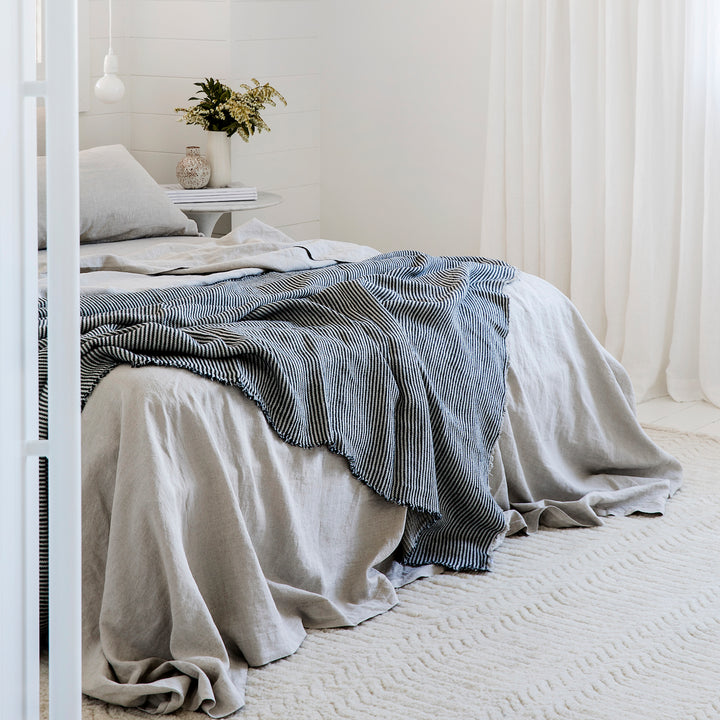 A bed dressed in a Linen Sheet Set in Smoke Grey, paired with a Mira Ellis Stripe Bedcover						