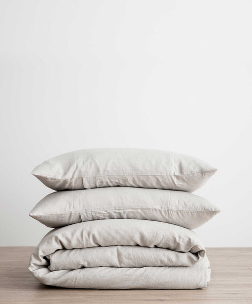 Stacked smoke grey linen duvet cover set with two pillows on wooden surface against white background