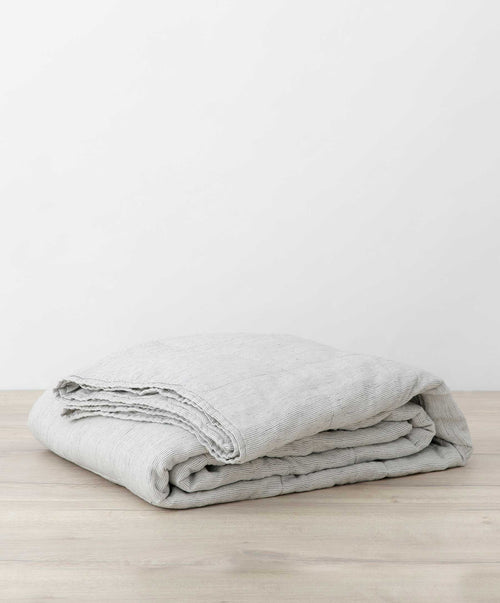 Quilted Bedcover - Pinstripe folded on wooden surface showing soft natural linen in muted tones The beauty of home