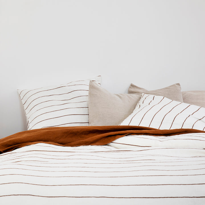 Close up of a bed dressed in Cedar Stripe, Natural and Cedar bedlinen.					