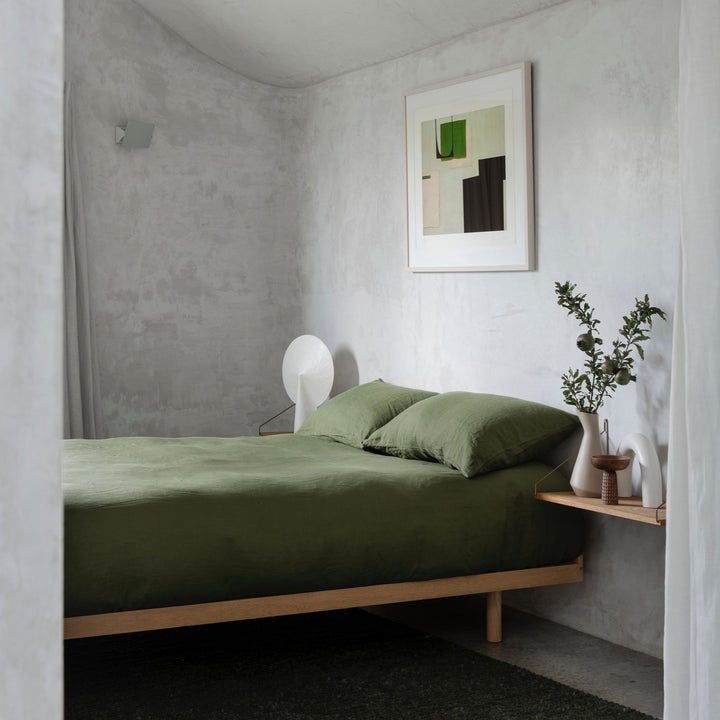 A bed dressed in Forest bed linen styled with a vase, greenery and modern artwork						