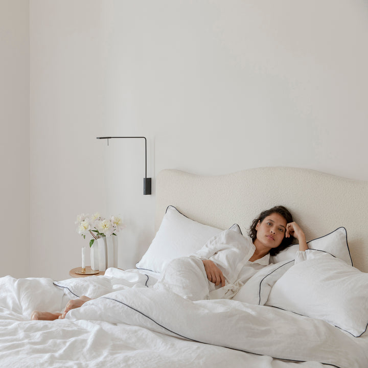 A woman relaxes on a cream bed dressed in White and Navy Piped bed linen.