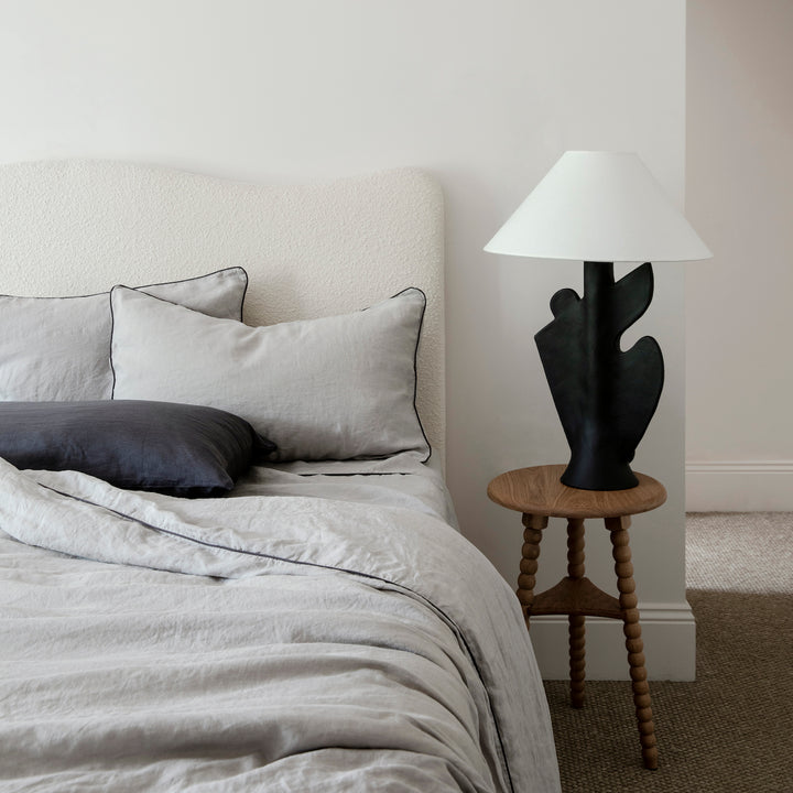 A cream bed dressed in Smoke Grey and Slate Piped bed linen, styled with Slate pillowcases							
