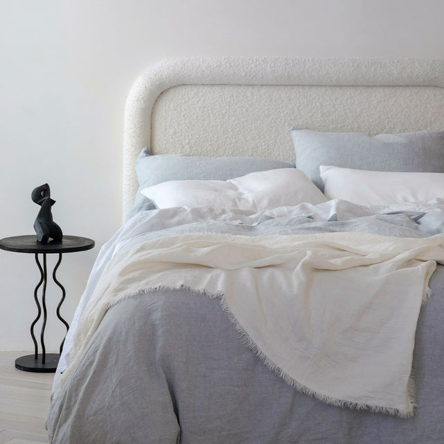 A bed dressed Sky and White bed linen, styled with a Freya Linen Throw in Snow and a black bedside table. Sizes: Double, Queen, King, Super King