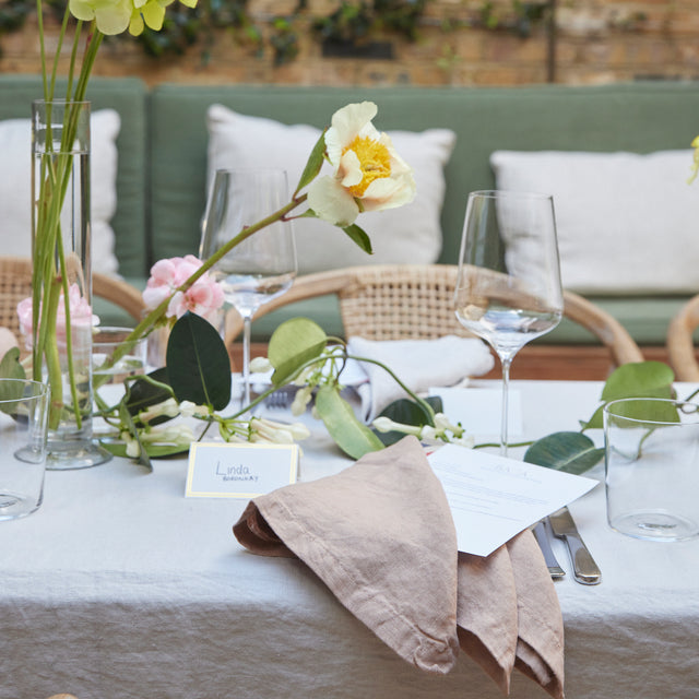 A close up of a dining table featuring a Smoke Gray Linen Tablecloth, paired with Fawn and Smoke Gray Linen Napkins