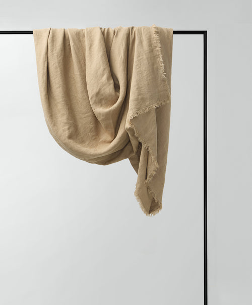 Freya Linen Throw - Biscuit draped on sleek black frame showcasing soft, natural linen fabric The beauty of home