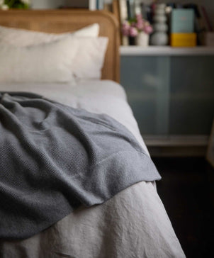 blanket draped over bed with beige duvet cover underneath
