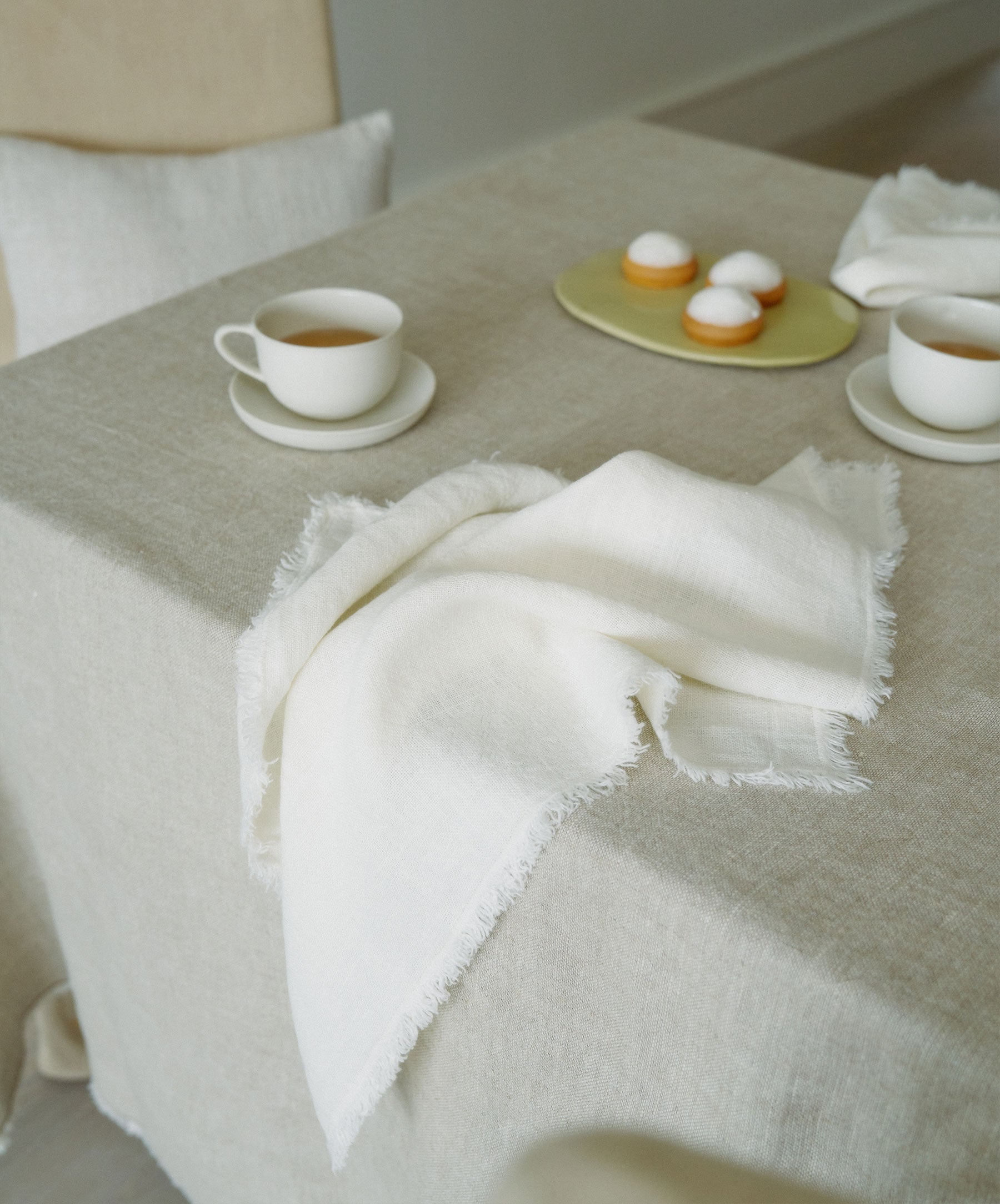 Fia Napkins - Ivory with softly fringed edges resting on natural linen tablecloth for timeless dining The beauty of home