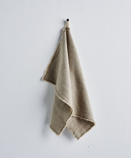 Fia Kitchen Towel - Natural hanging simply on black hook showing soft textured linen with subtle fringed edges The beauty of home