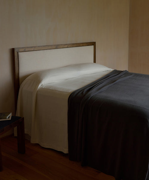 100% NZ Merino Wool Blanket - Slate draped over a modern bed with cream linens in a minimalist bedroom.