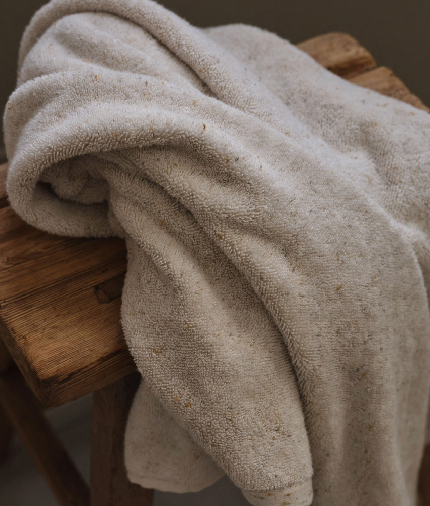Creamy textured linen throw casually draped over rustic wooden bench with natural folds and creases