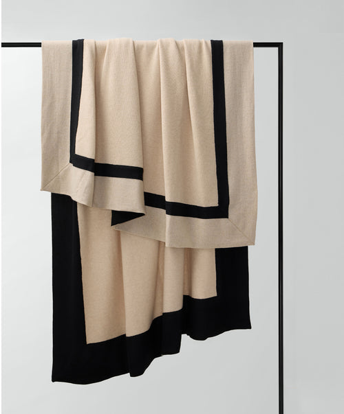Aria Cashmere Throw in beige and black, draped on a black metal rack, showcasing its soft, luxurious texture.