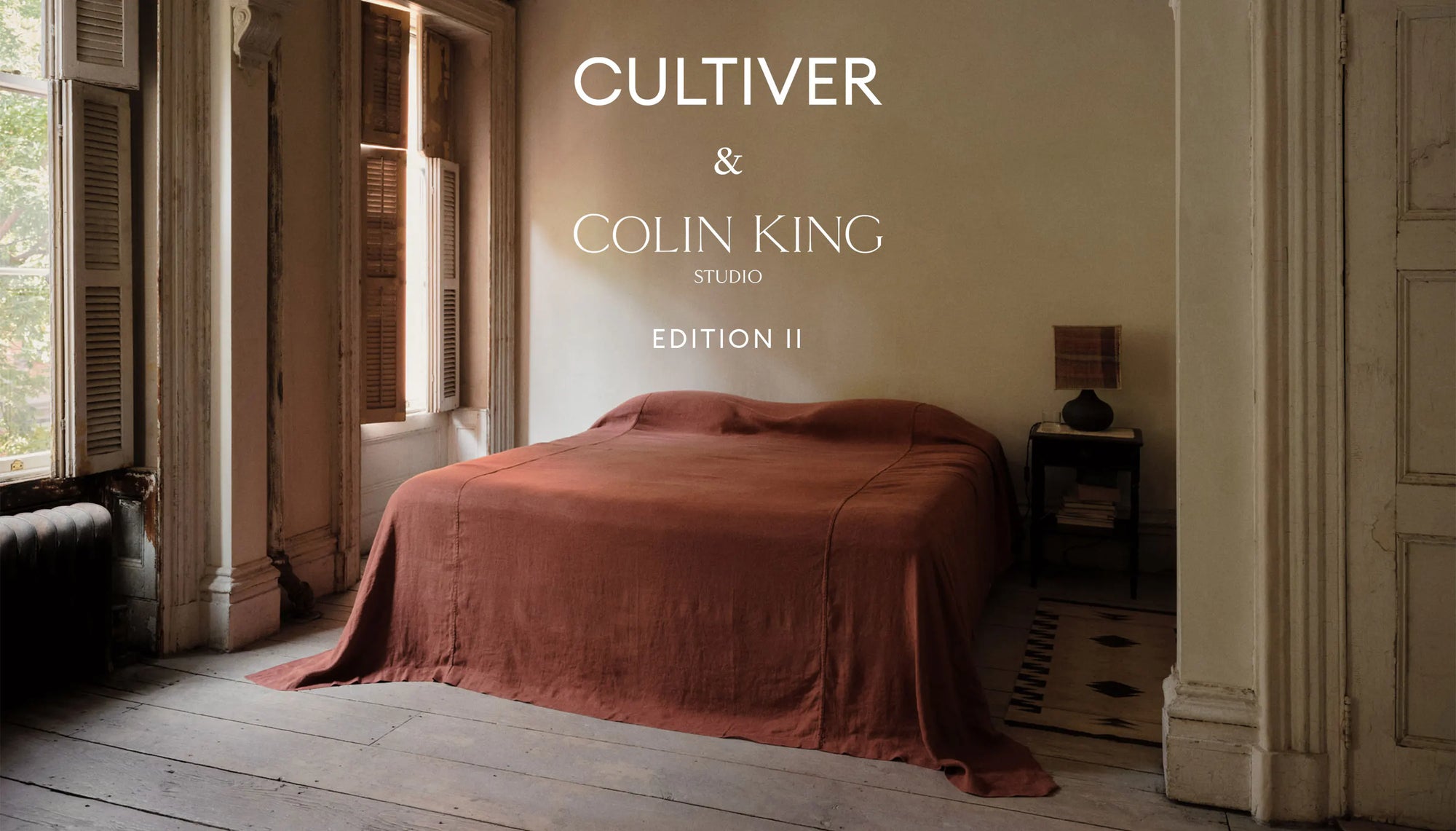 A rustic bedroom scene with a bed dressed in rust-colored bedding, set in an old stone room with wooden floors and shutters. White text at the top reads 'CULTIVER & COLIN KING STUDIO EDITION II'.