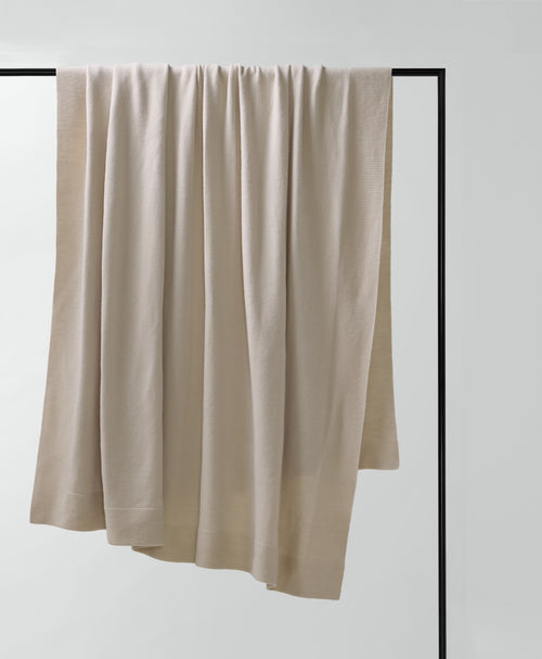 Beige blanket draped over a black rod against a white background