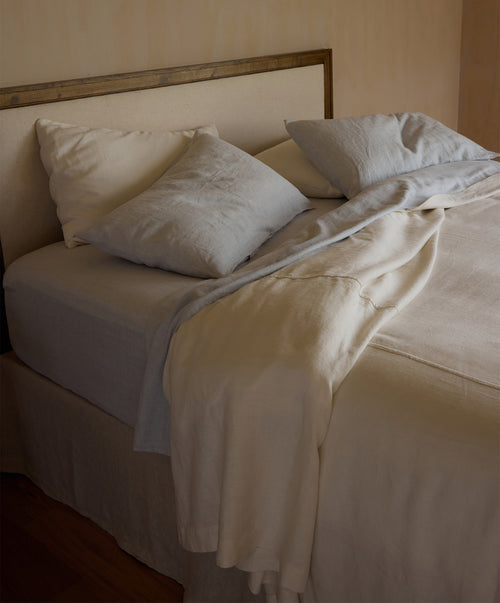 Neatly made bed with white and sky pillows and an ivory bedcover in a softly lit room.