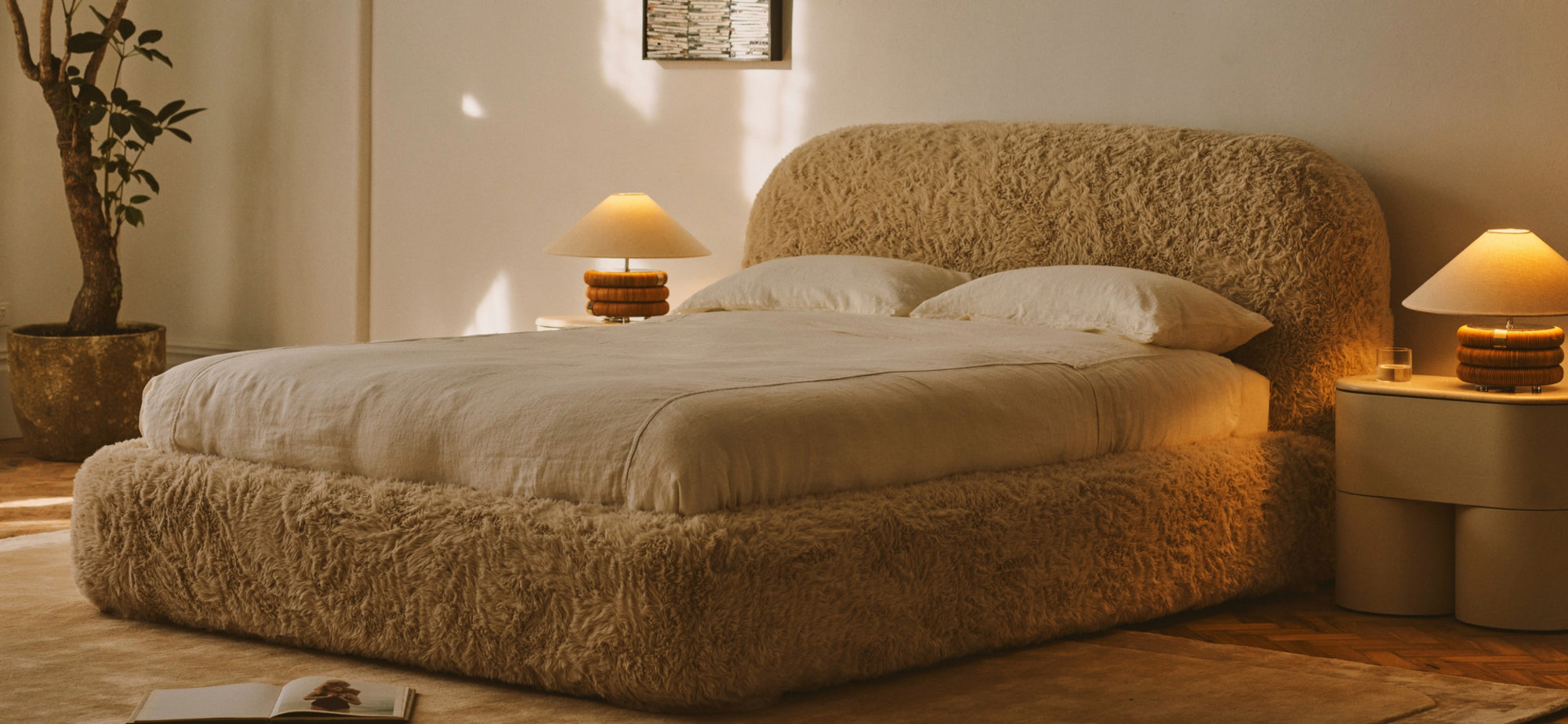 Cozy bedroom with a plush textured bed frame, neutral bedding, warm lamps, and soft natural light through window