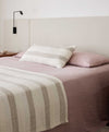 A modern bed styles with dusk linen sheets and pillowcase, lumbar striped cushion and striped throw.