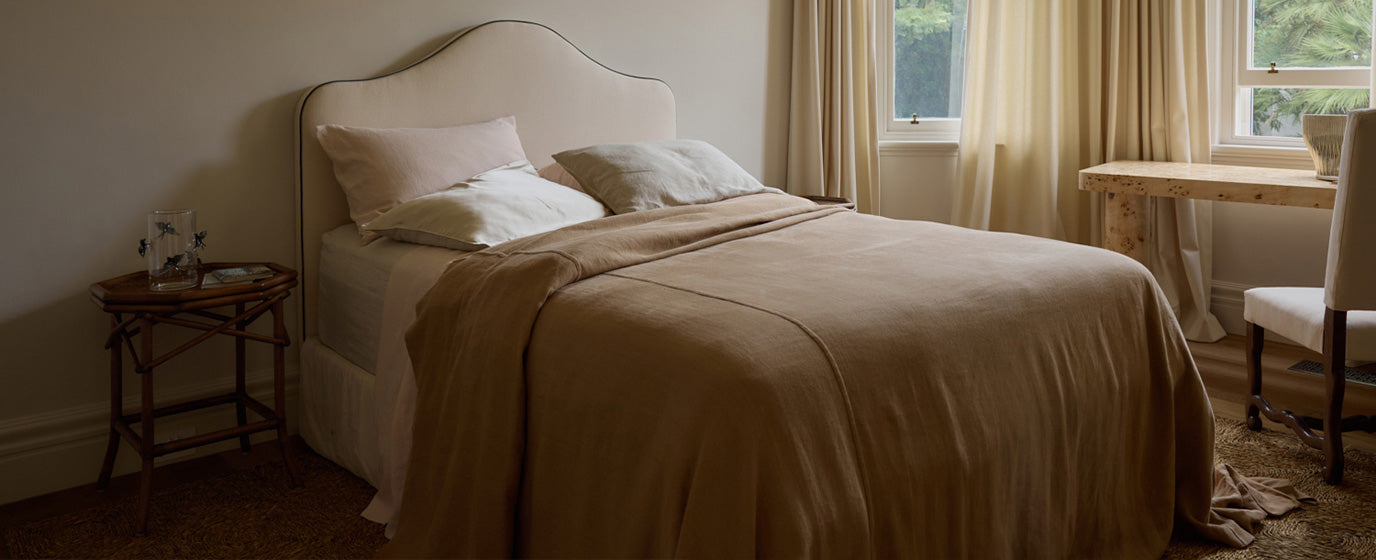 Neatly made bed with beige bedding in a softly lit bedroom.