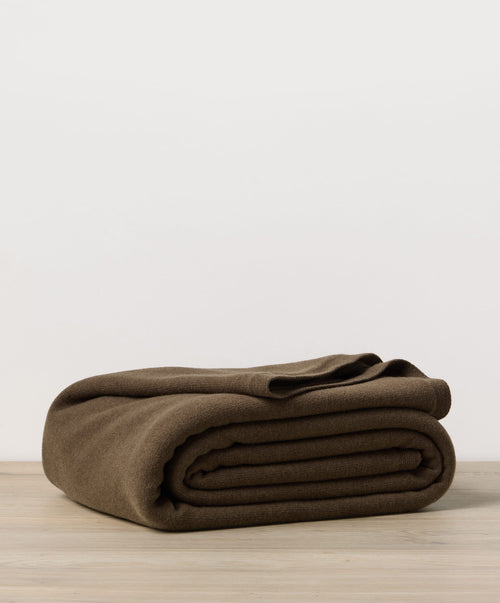 Folded brown blanket on a wooden surface with a light gray background