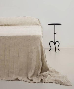Beige textured blanket draped over a bed with a black metal side table in the background.