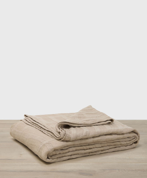Folded beige blanket on a wooden surface with a light gray background