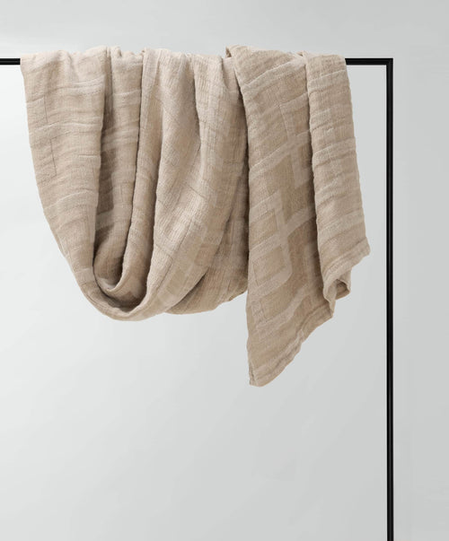 Beige textured blanket draped over a black metal frame against a light gray background