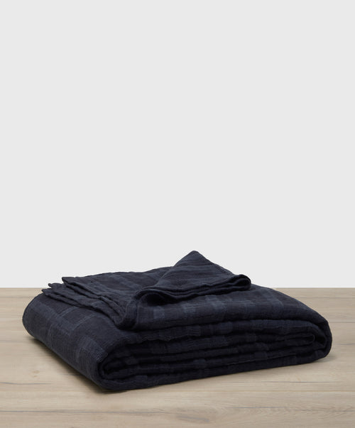 Folded dark blue blanket on a wooden surface with a light gray background