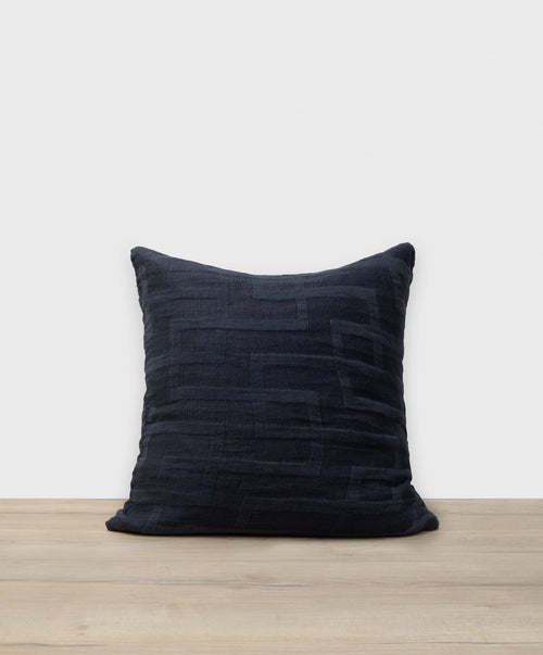 Dark blue textured pillow on a wooden surface with a white background