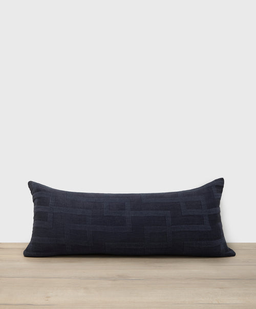 Navy blue pillow with geometric pattern on a wooden surface and light gray background