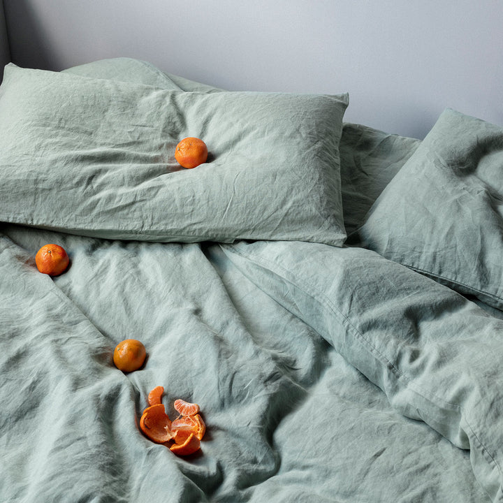A bed dressed in Sage bed linen, styled with mandarins. Sizes: Single, Queen, King