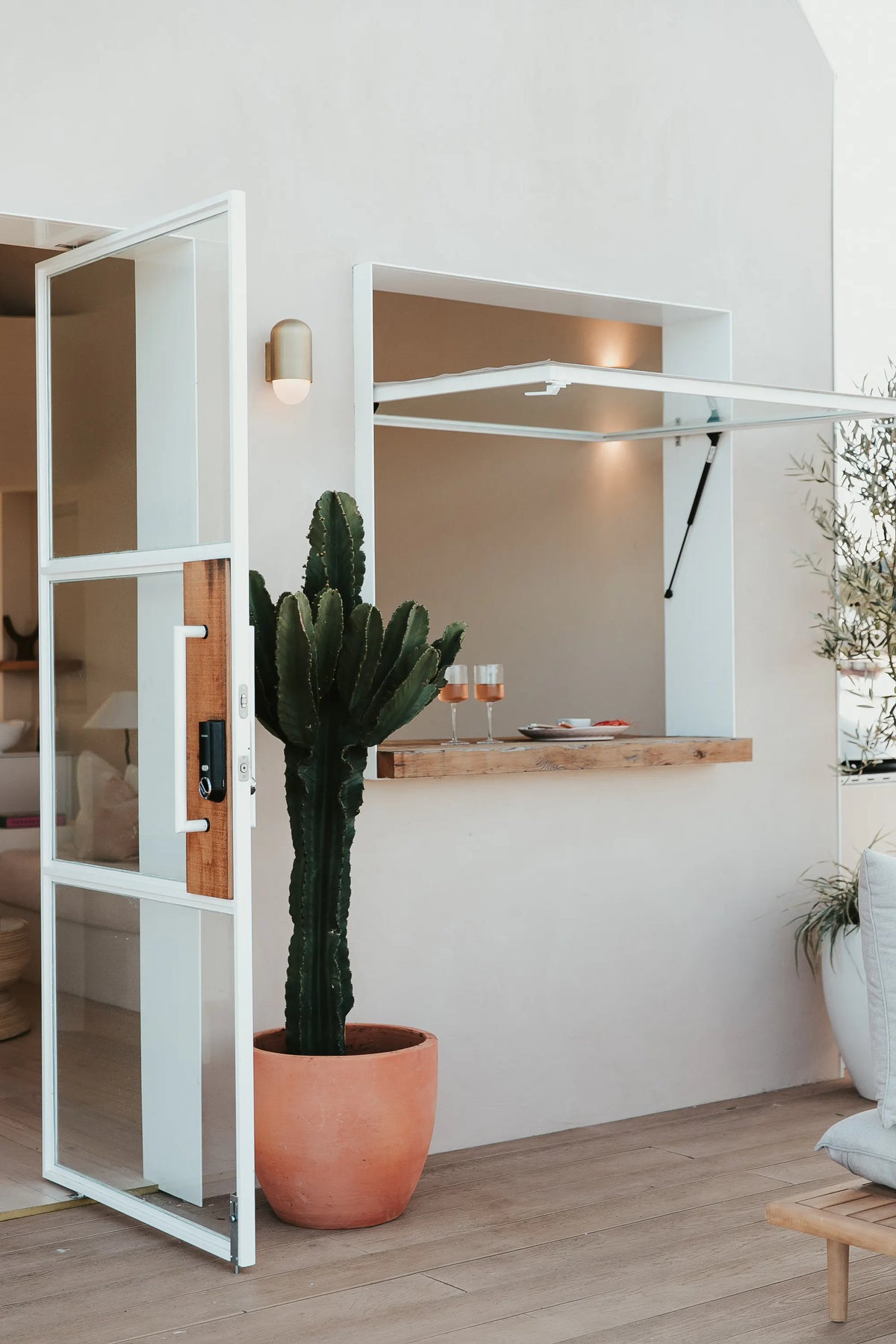 A modern white wall-mounted window seat with a wooden shelf and built-in lighting, shown in a bright interior with a large potted cactus and light wood flooring.