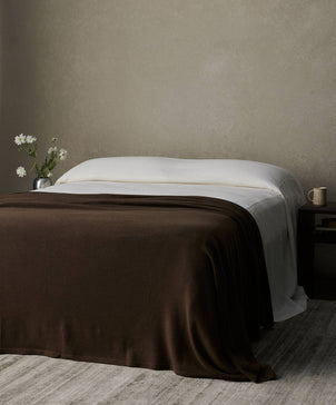 Bed with brown blanket and white duvet against a beige wall