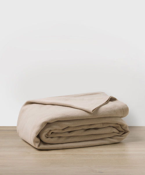 100% NZ Merino Wool Blanket - Oatmeal folded on wooden surface showing soft, finely knitted wool texture.