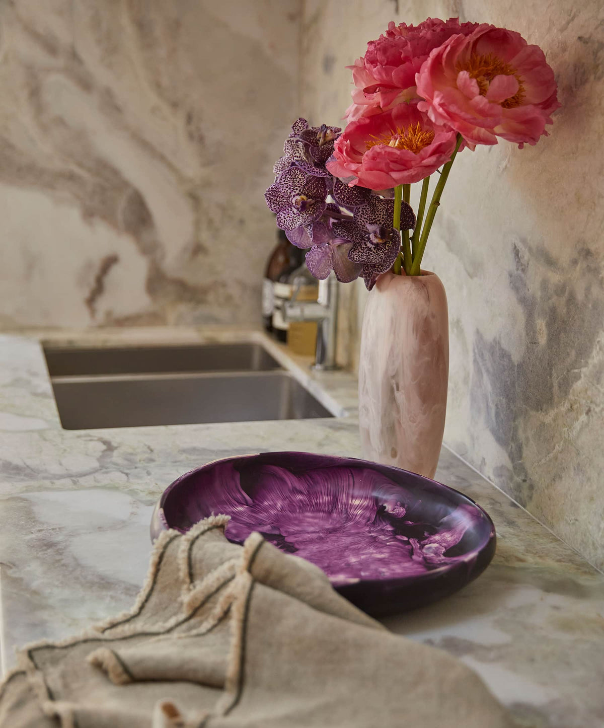 Purple marbled plate on a marble countertop with a vase of flowers and kitchen background