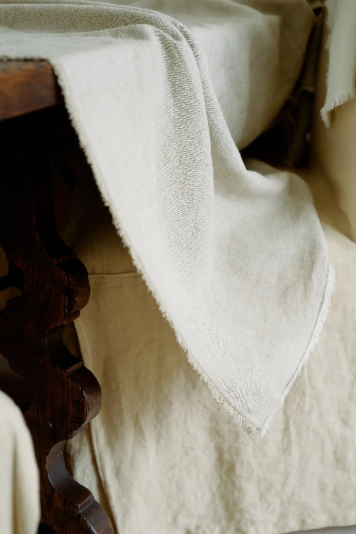 Light neutral linen cloth with subtle texture draped over dark carved wooden furniture edge