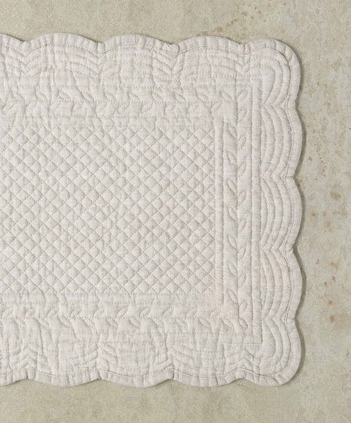 Quilted white fabric with a scalloped edge on a beige background