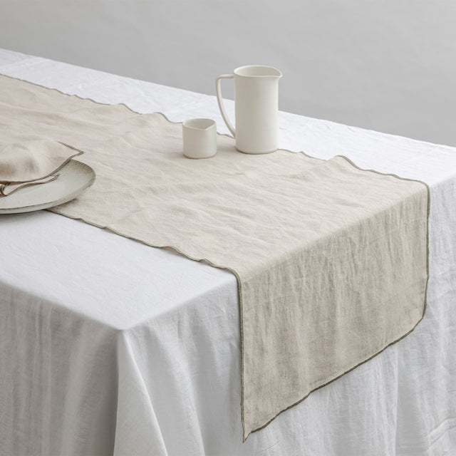 Cara Edged Table Runner in Olive on a Linen Tablecloth in White. Size: 50cm x 200cm, 50cm x 300cm