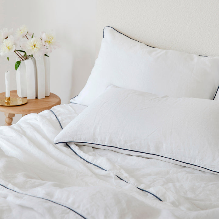 A close up of a bed dressed in White and Navy Piped bed linen