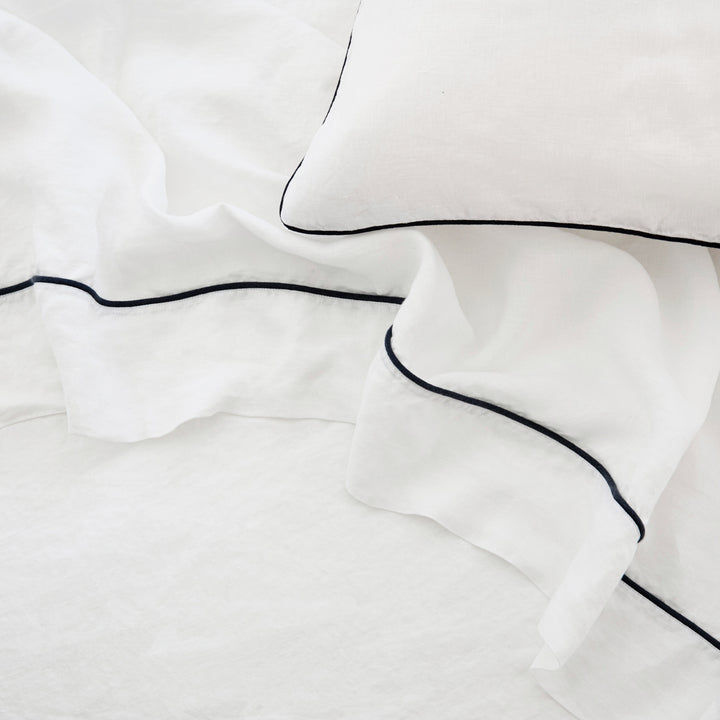 A close up of a Piped Linen Flat Sheet in White and Navy