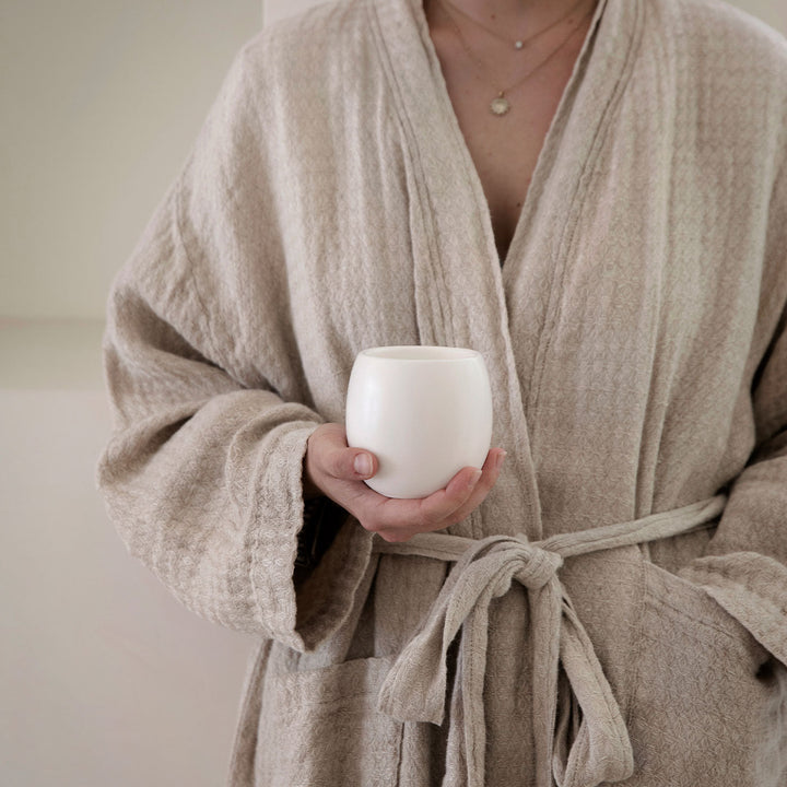 Close up view of Waffle Robe in Natural. Model is holding a Circe Candle. Sizes: S/M and M/L